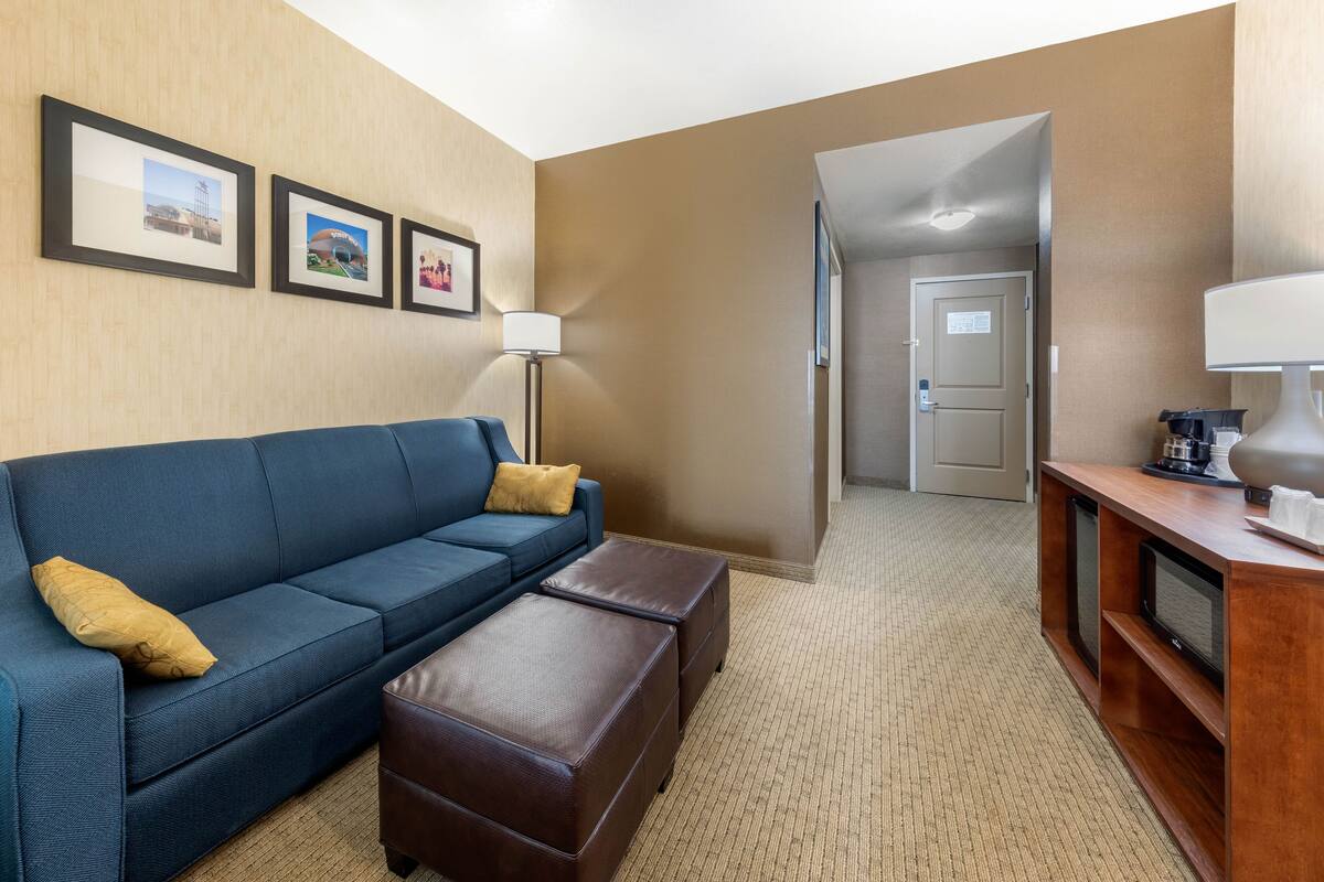 A hotel room with a blue sofa, a wooden coffee table, a lamp, and framed pictures on the wall.