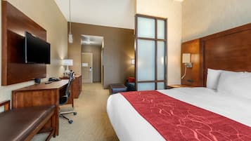 A hotel room with a bed, a desk, a TV, a chair, and a bathroom door.