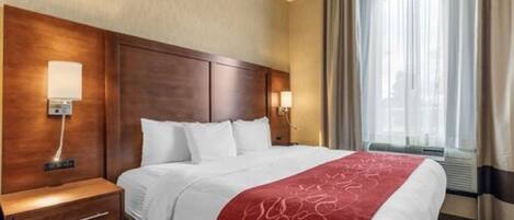 Quarto de hotel com uma cama grande, duas mesas de cabeceira, um painel de cama de madeira e uma janela com cortinas.
