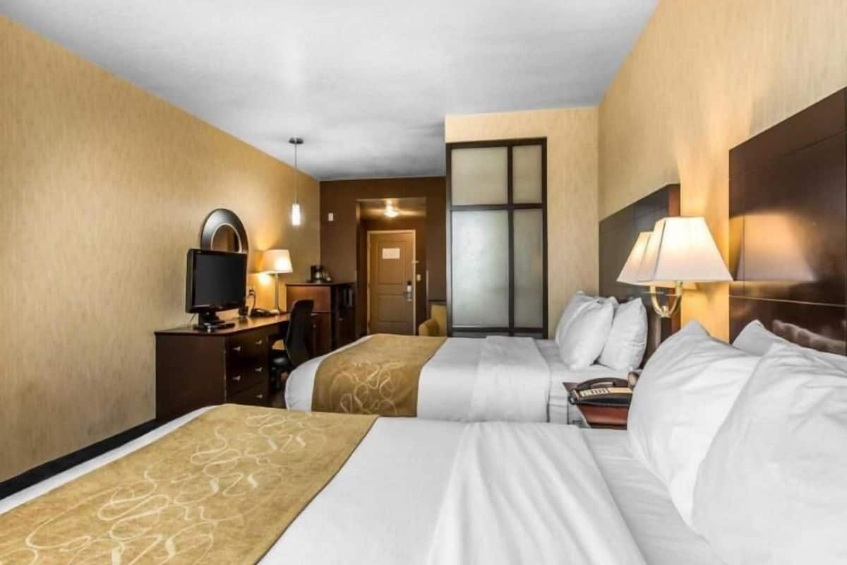 Habitación de hotel con dos camas, un escritorio con computadora, una silla y una puerta que da a otra habitación.
