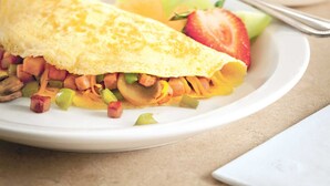 A breakfast plate with an omelette, vegetables, and a glass of orange juice.