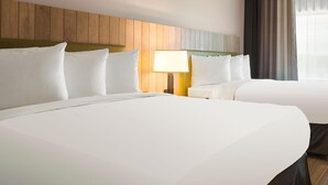 Een hotelkamer met twee bedden, een houten hoofdbord, een bedlampje en een raam met gordijnen.