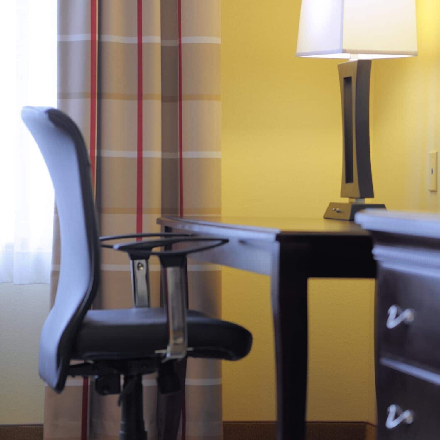 Une chambre d’hôtel avec un bureau noir, une chaise et une lampe.
