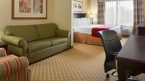 Een hotelkamer met een groene bank, een gestreepte fauteuil, een bed met een rode deken, een bureau en een stoel.