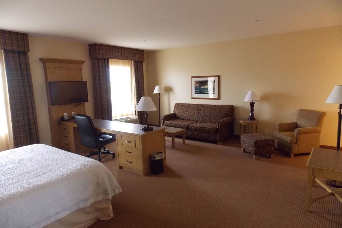 Ein Hotelzimmer mit Bett, Schreibtisch, Sessel, Sofa und zwei Lampen.