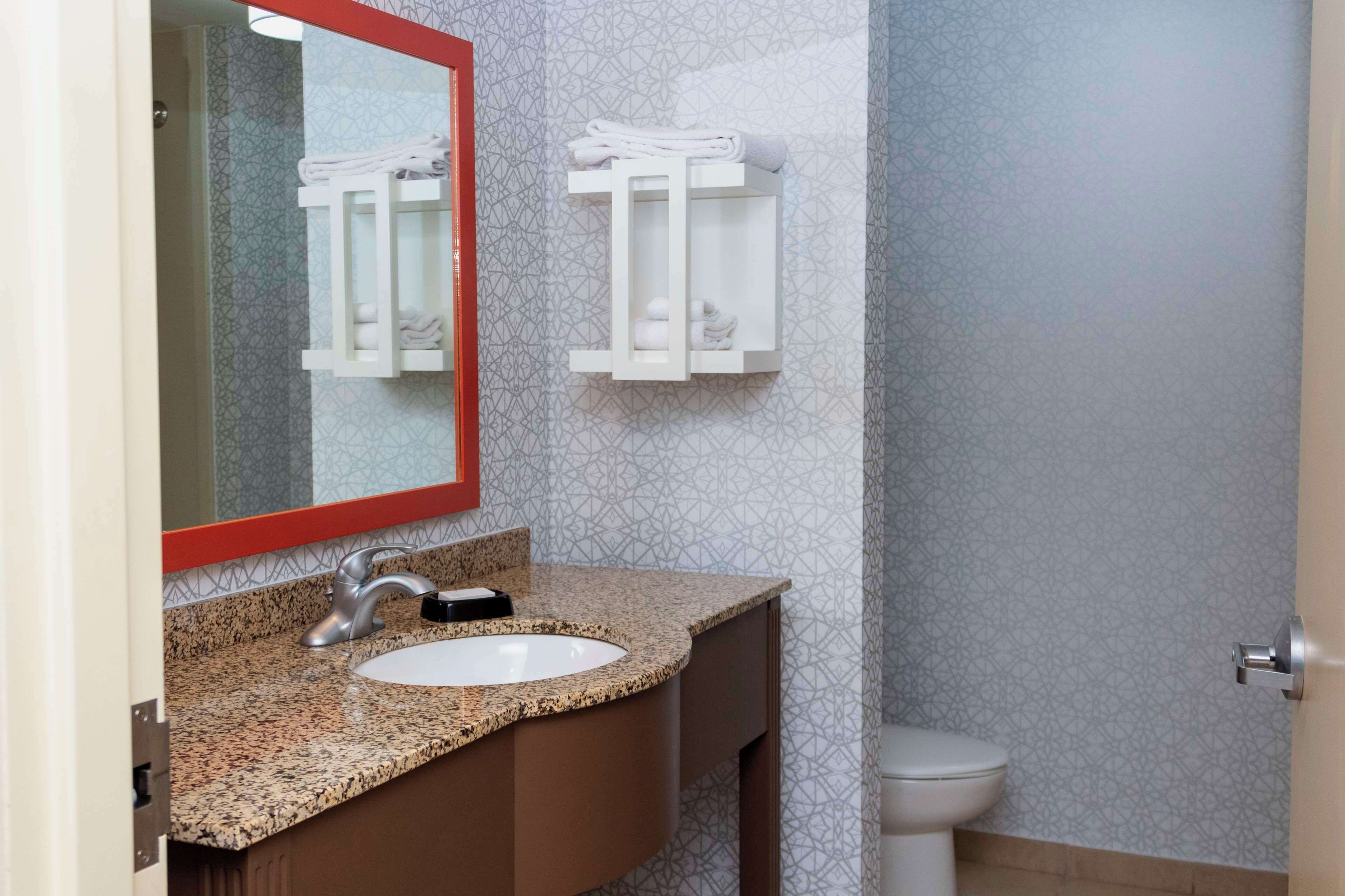 A bathroom with a granite countertop sink, a mirror with a red frame, and two towel racks on the wall.