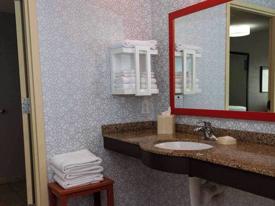 A bathroom with a sink, mirror, towel rack, and a small table with folded towels.