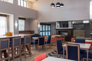 A modern hotel lobby with a mix of seating areas, including tables and chairs, and a prominent sign reading "WELCOME TO THE COWBOY STATE". - Hampton Inn & Suites Riverton (Riverton)