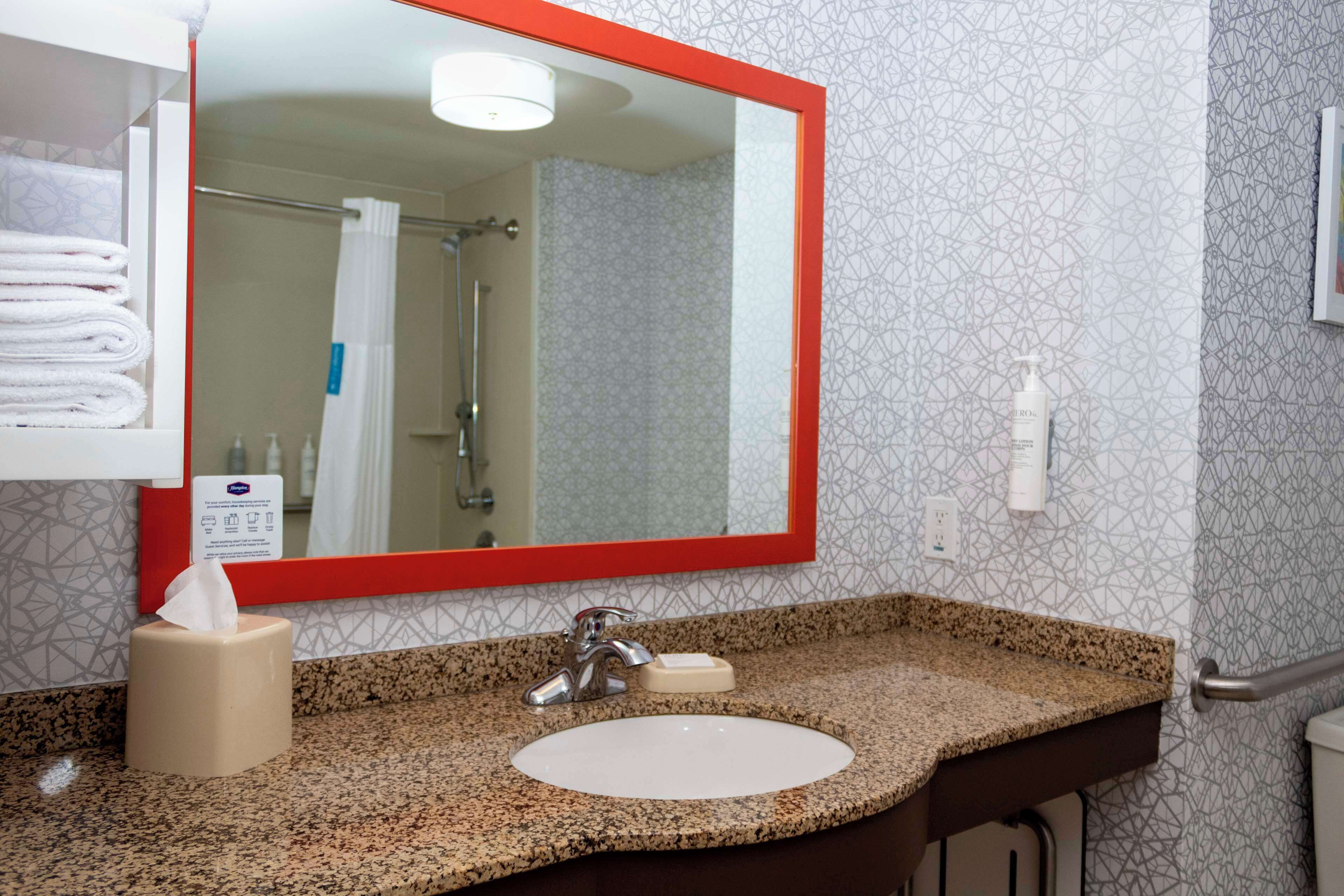 Une salle de bain avec un comptoir en granit, un lavabo blanc, un miroir à cadre rouge et un distributeur de serviettes.
