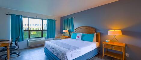 Habitación de hotel con una cama grande, un escritorio, una silla y una mesita de noche con lámpara.