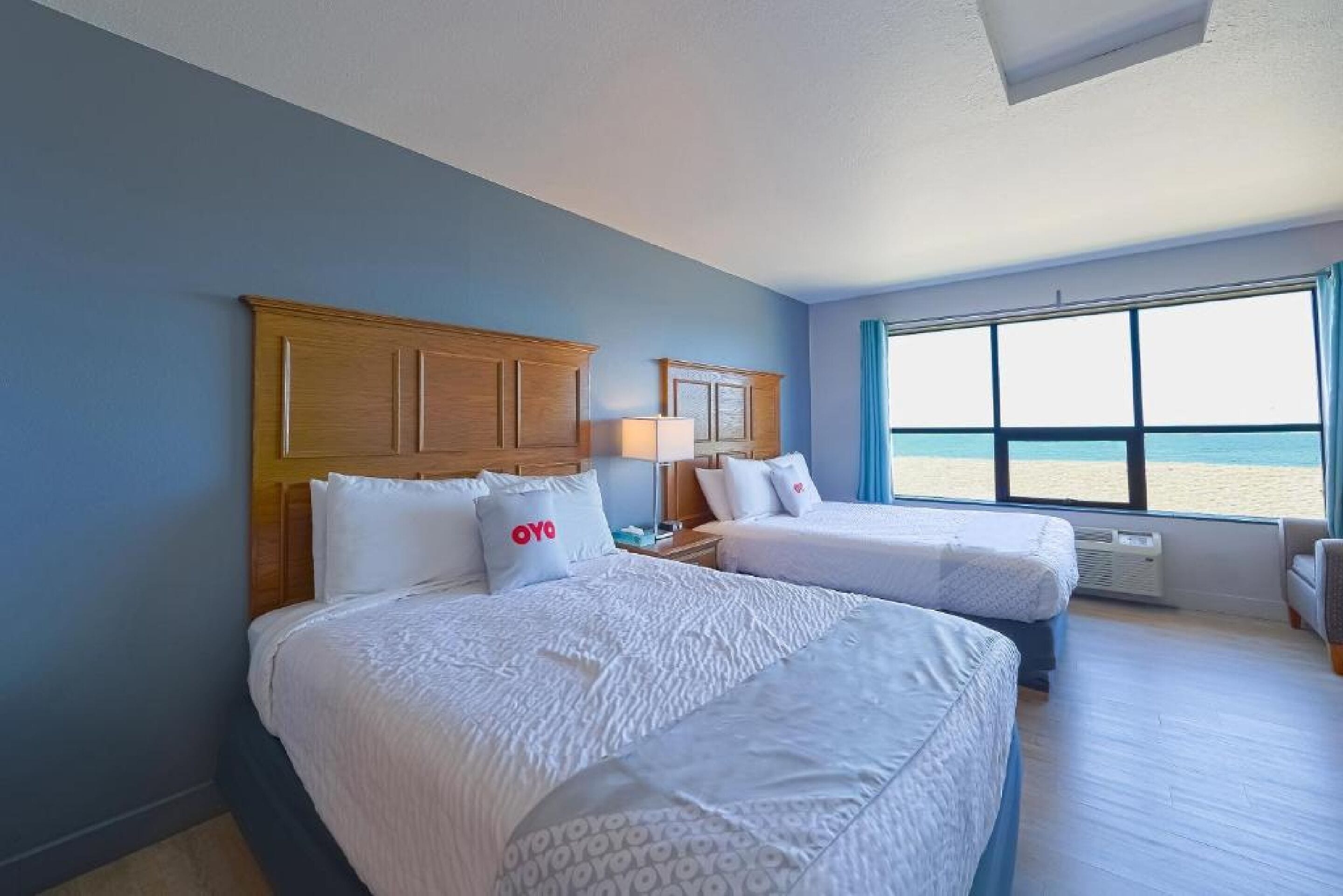 A hotel room with two beds, a large window with a beach view, and a wooden headboard.