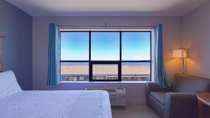 A hotel room with a large window, a bed, a chair, and a desk. - Waves Hotel NYE Beach - Newport OR (Newport)