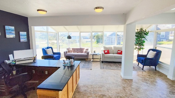 A spacious living room with a large dining table, two sofas, and a coffee table. There are large windows providing natural light and a view of the outside. - Waves Hotel NYE Beach - Newport OR (Newport)