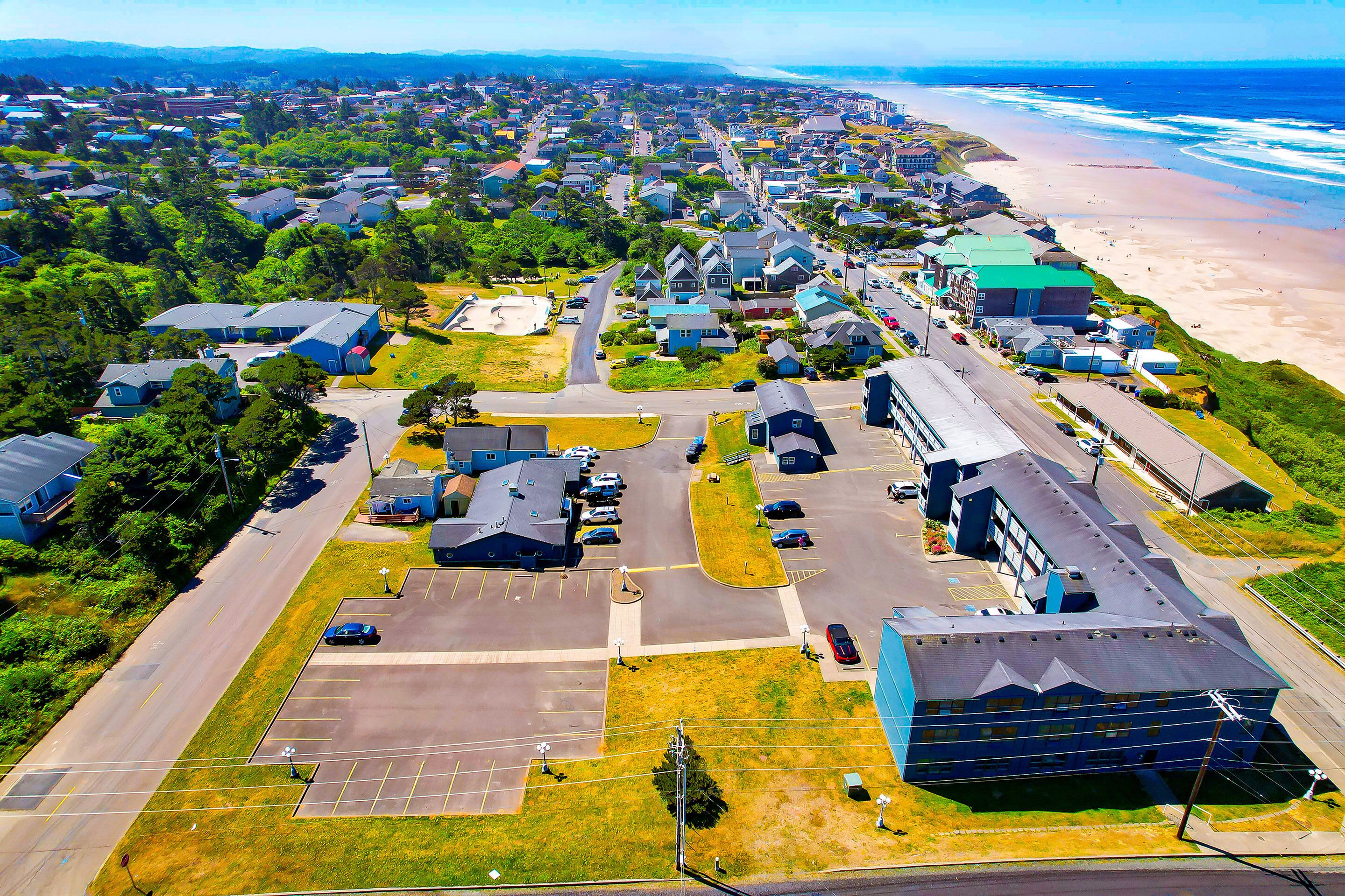 An aerial view of a coastal residential area with houses, a beach, and a parking lot.