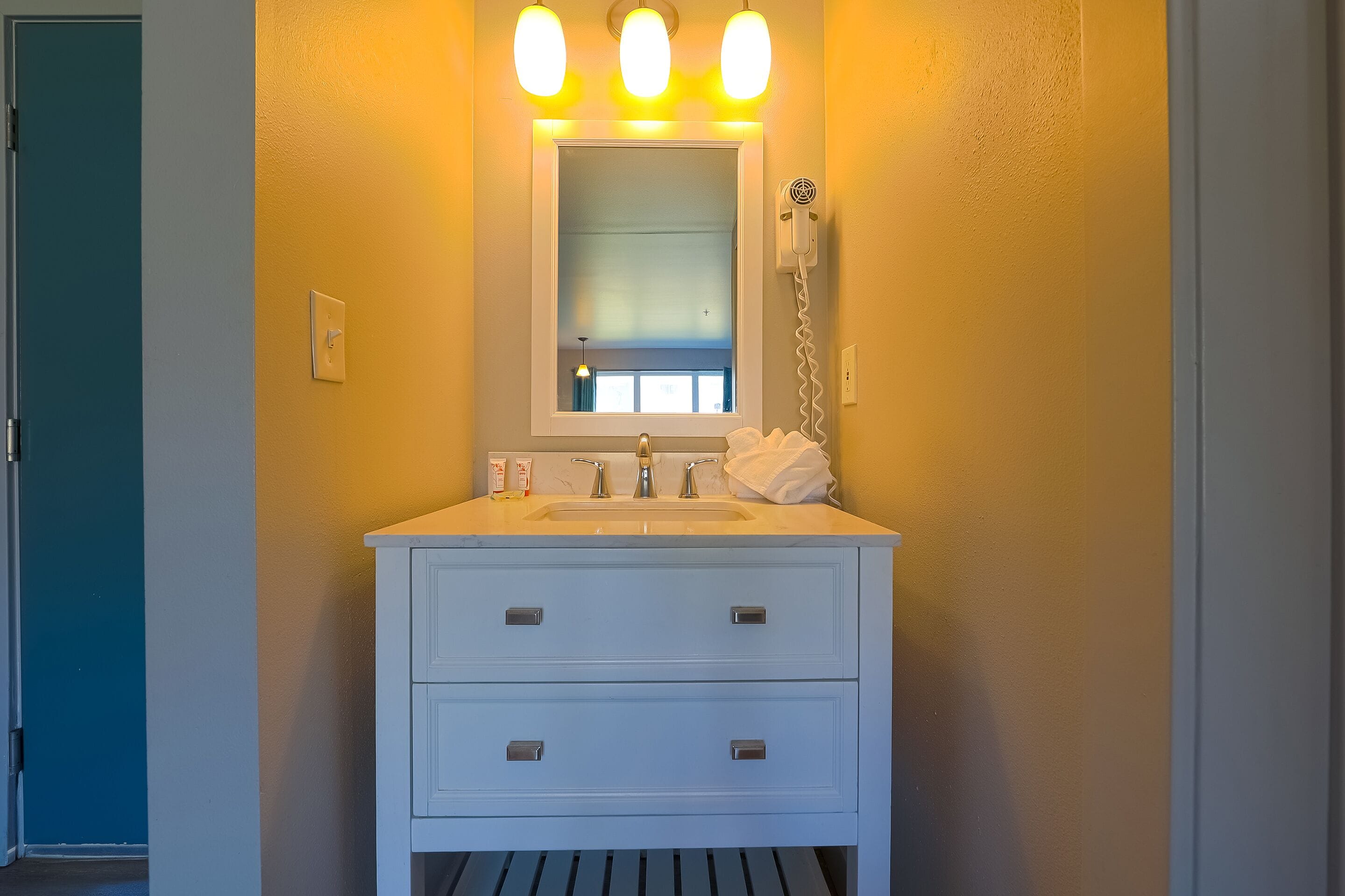A bathroom with a white vanity, a mirror, and a hairdryer on the wall.