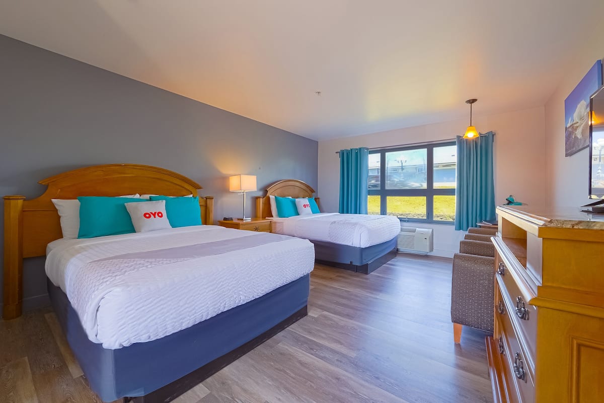 Une chambre d’hôtel avec deux lits, une commode en bois, un bureau et une grande fenêtre avec des rideaux.