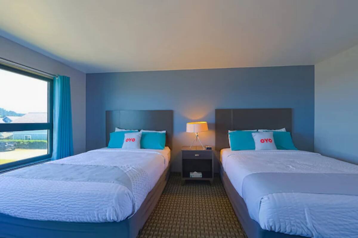 Une chambre d’hôtel avec deux lits, chacun doté d’une tête de lit, d’une table de chevet avec une lampe et d’une fenêtre avec des rideaux.
