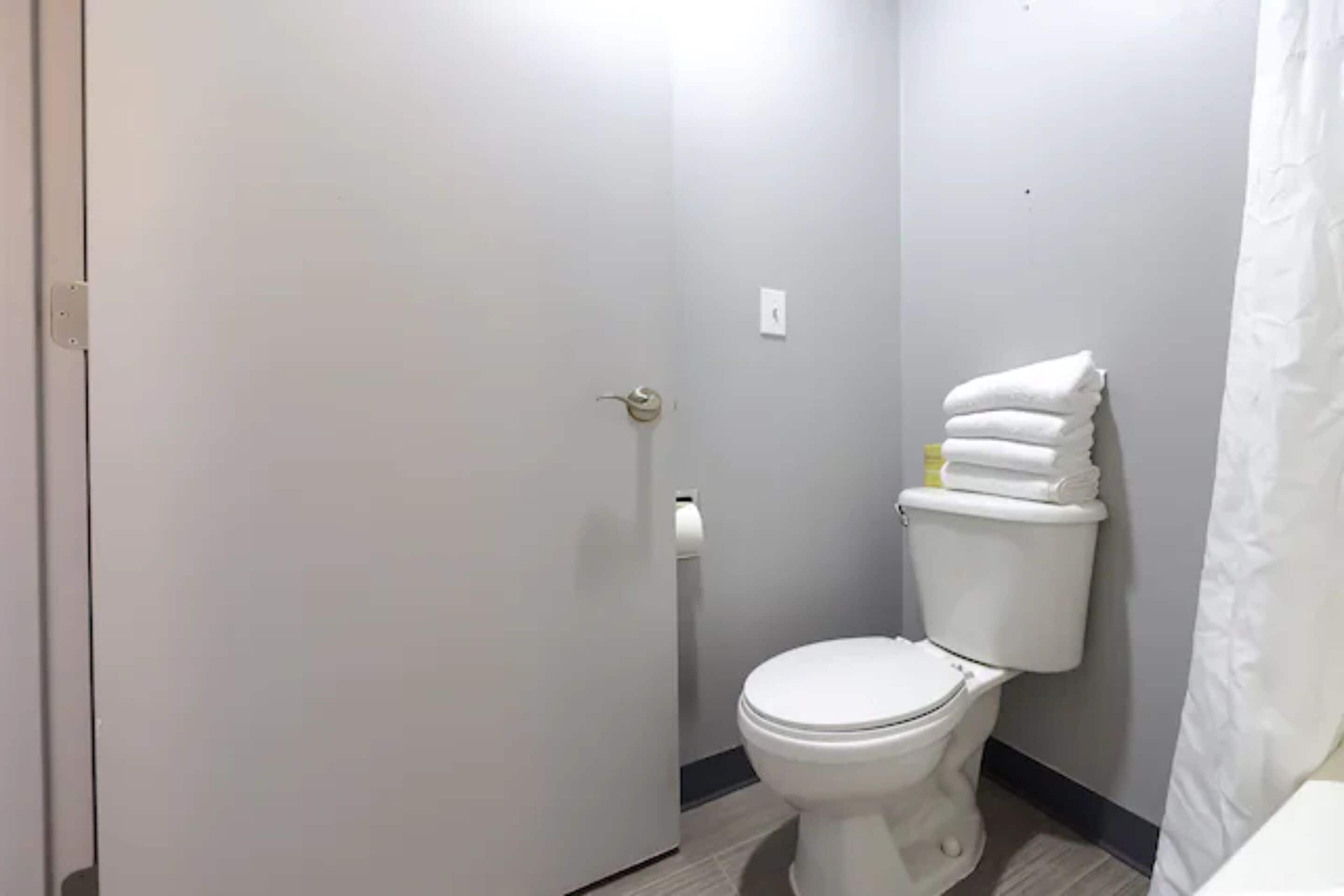 A bathroom with a toilet, a towel stack, and a shower curtain.