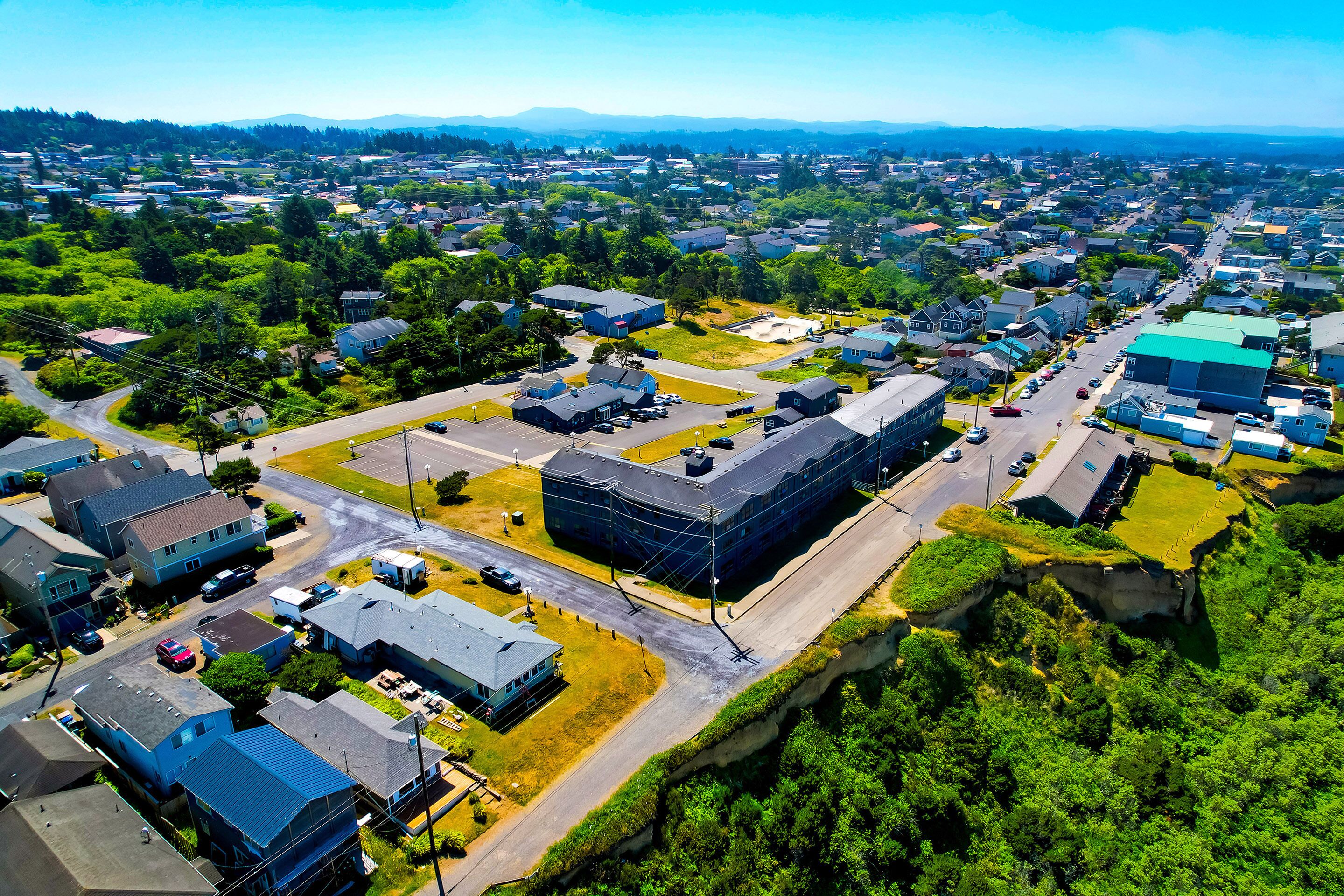 An aerial view of a residential area with houses, roads, and a large building with a green roof.