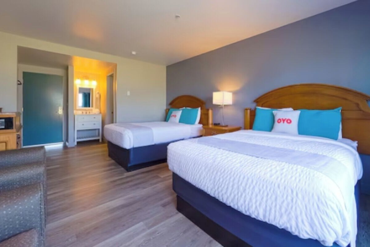 A hotel room with two beds, a sitting area, a vanity with a mirror, and a nightstand with a lamp.