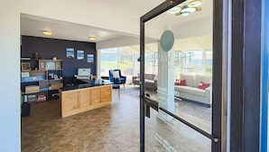 A modern hotel lobby with a reception desk, seating area, and large windows offering a view of the outdoors. - Waves Hotel NYE Beach - Newport OR (Newport)