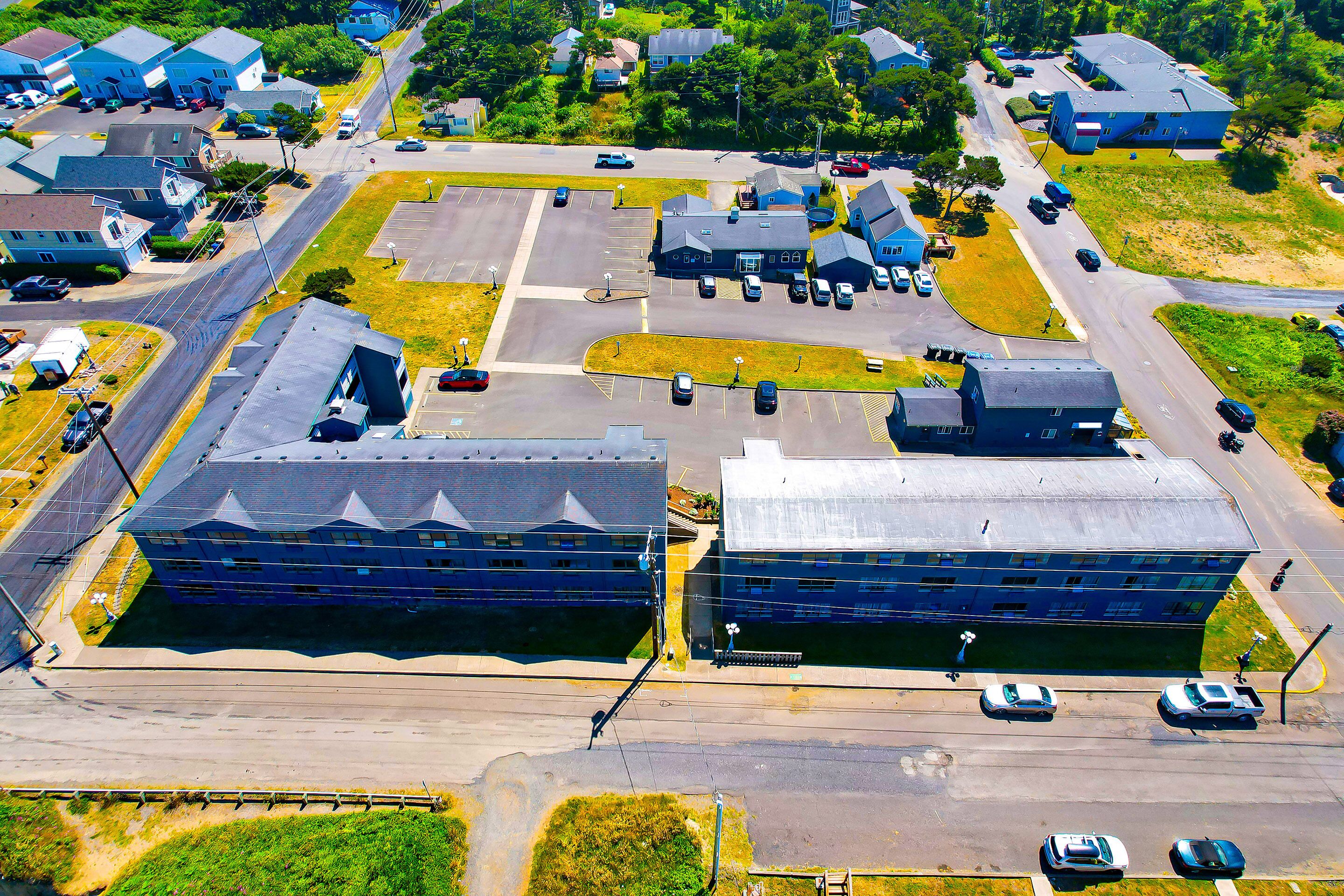 An aerial view of a parking lot with several buildings, including a large blue structure and a smaller white building.