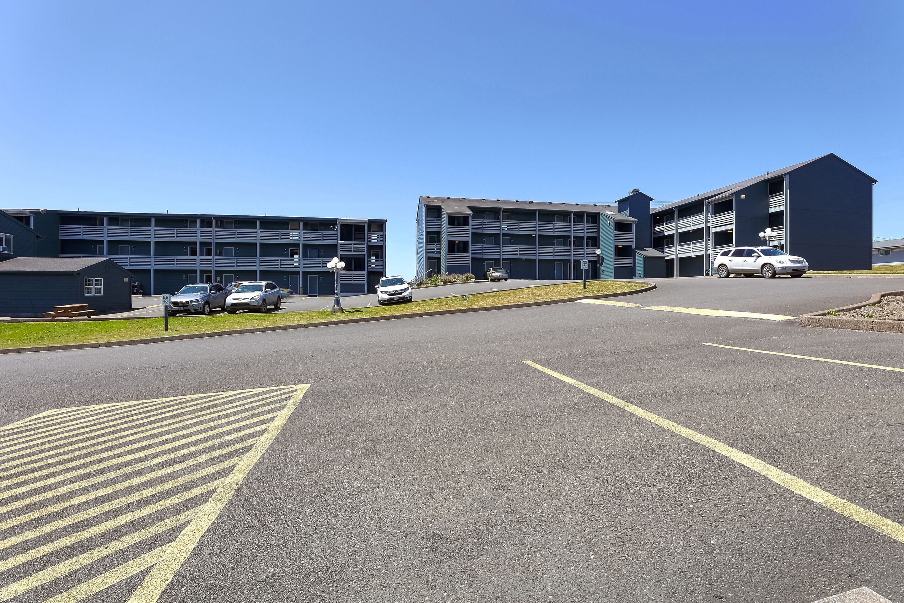 Un parking avec plusieurs voitures, un bâtiment doté de nombreuses portes de garage et un ciel bleu dégagé.