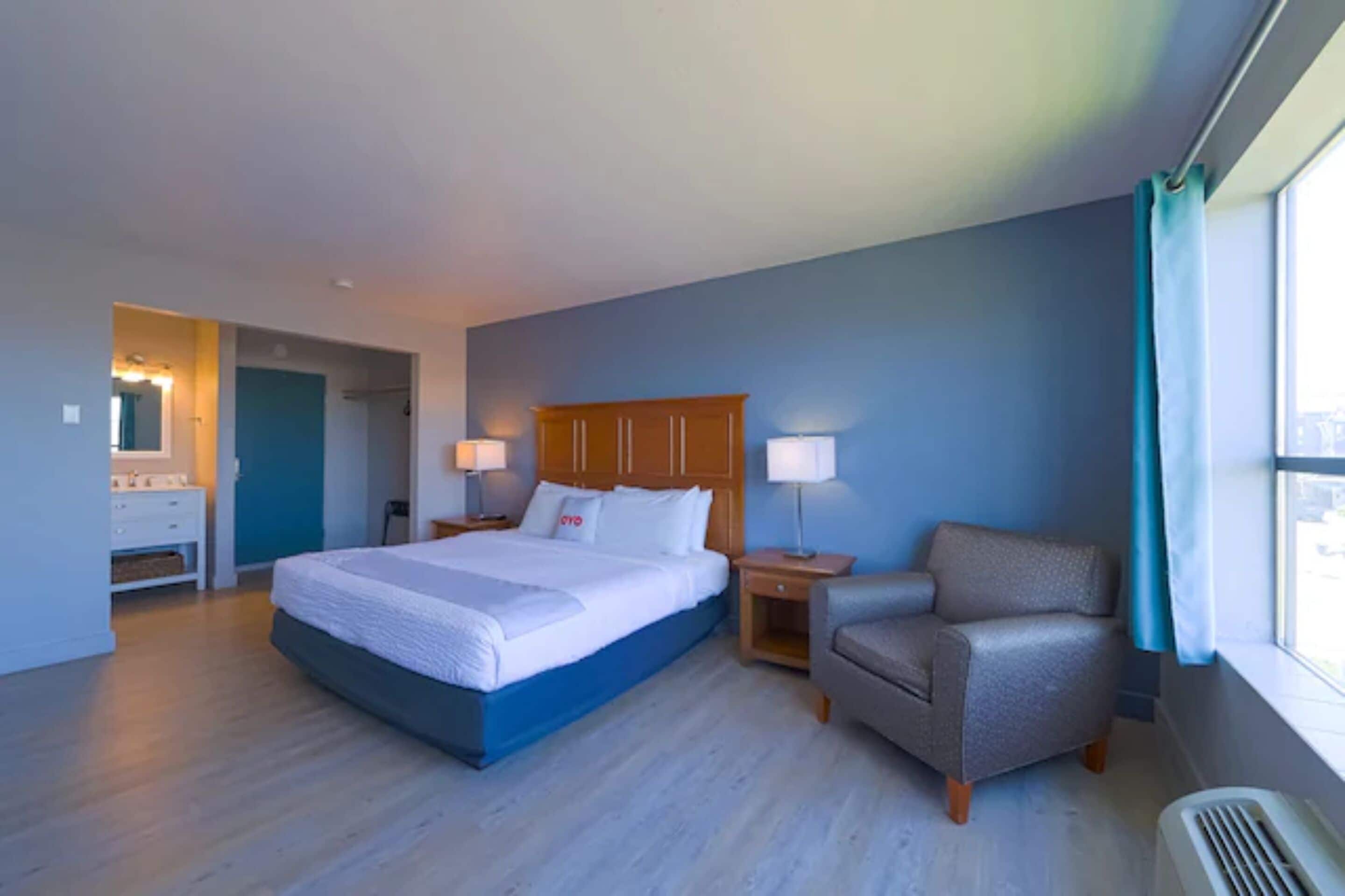 A hotel room with a large bed, a chair, a nightstand, and a window with curtains.