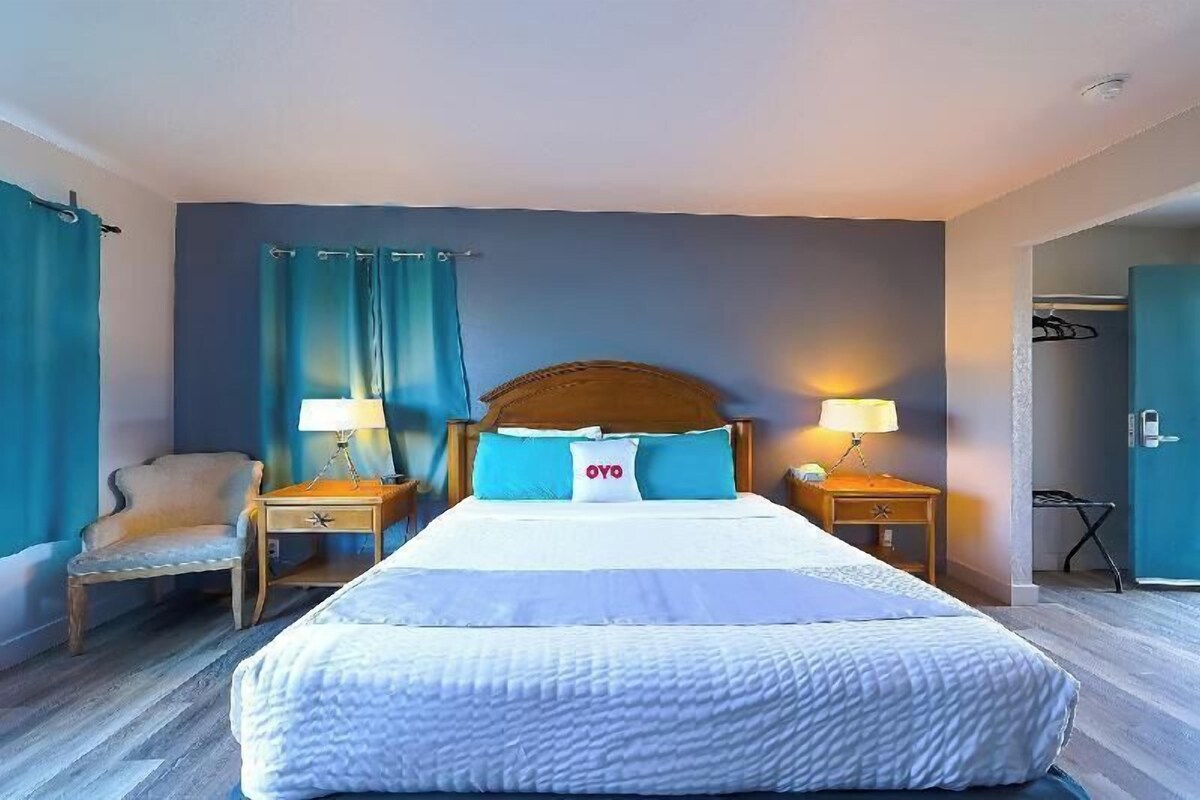 A hotel room with a large bed, two bedside tables with lamps, a chair, and a wardrobe.