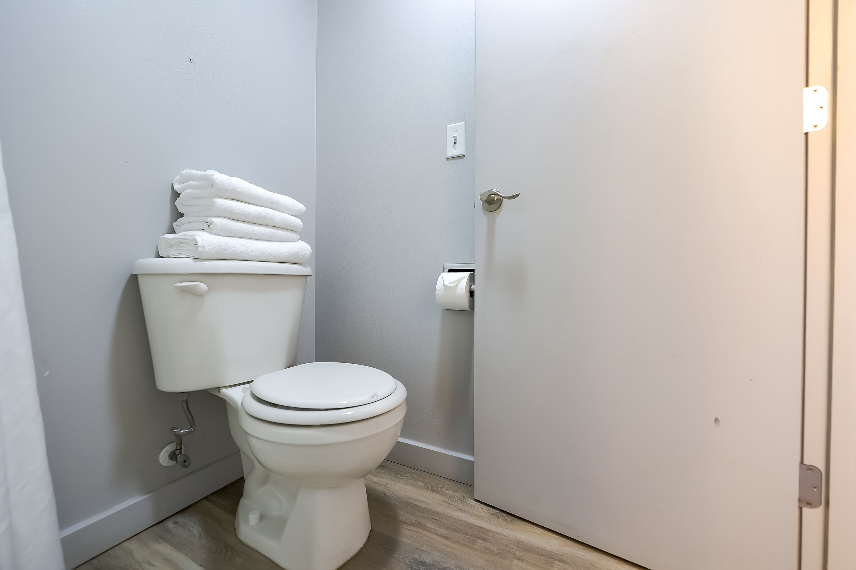 A small, clean bathroom with a toilet, a stack of white towels, and a toilet paper holder.