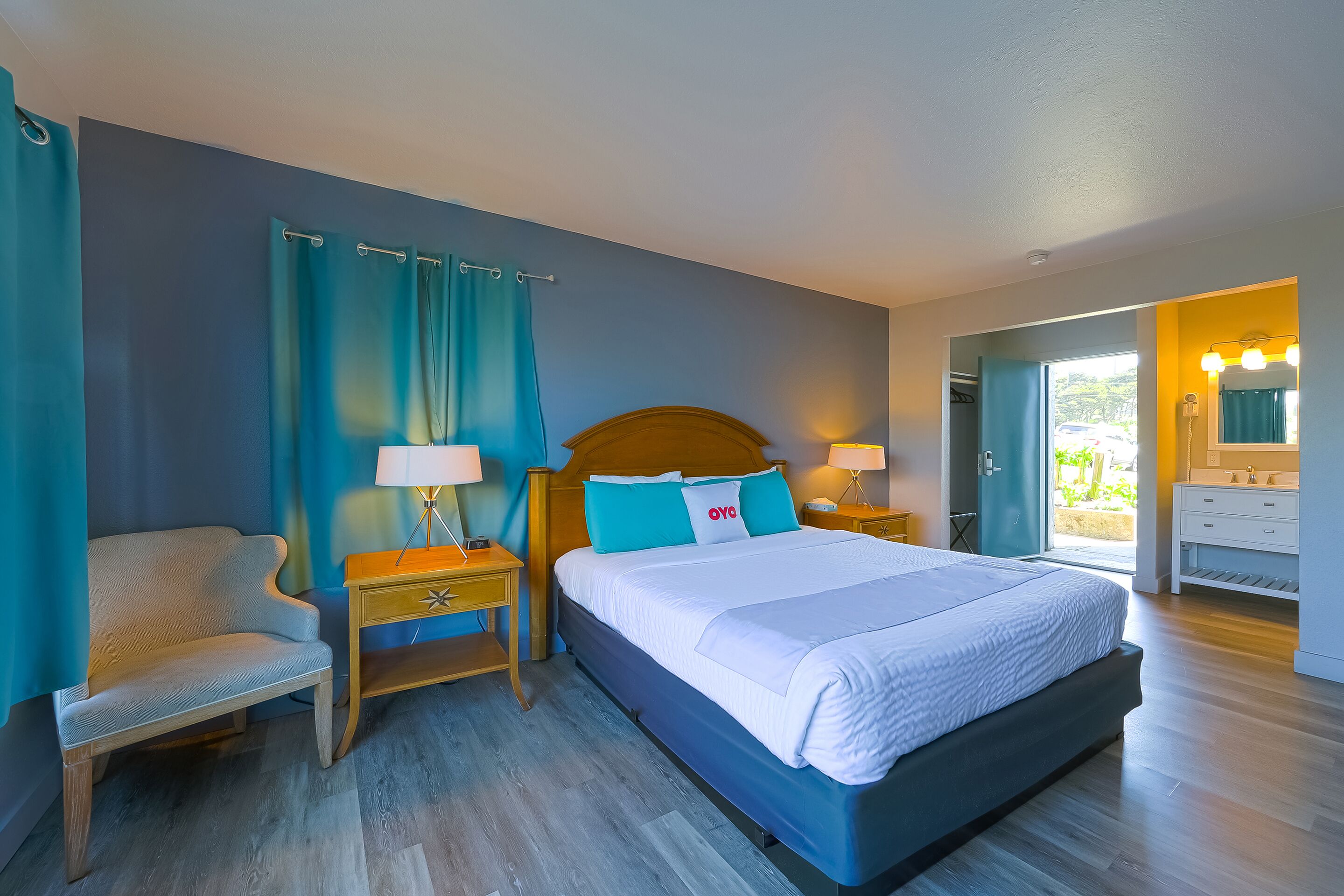 Ein Schlafzimmer mit einem großen Bett, einem Nachttisch, einem Sessel und einem Badezimmer mit Spiegel und Waschbecken.