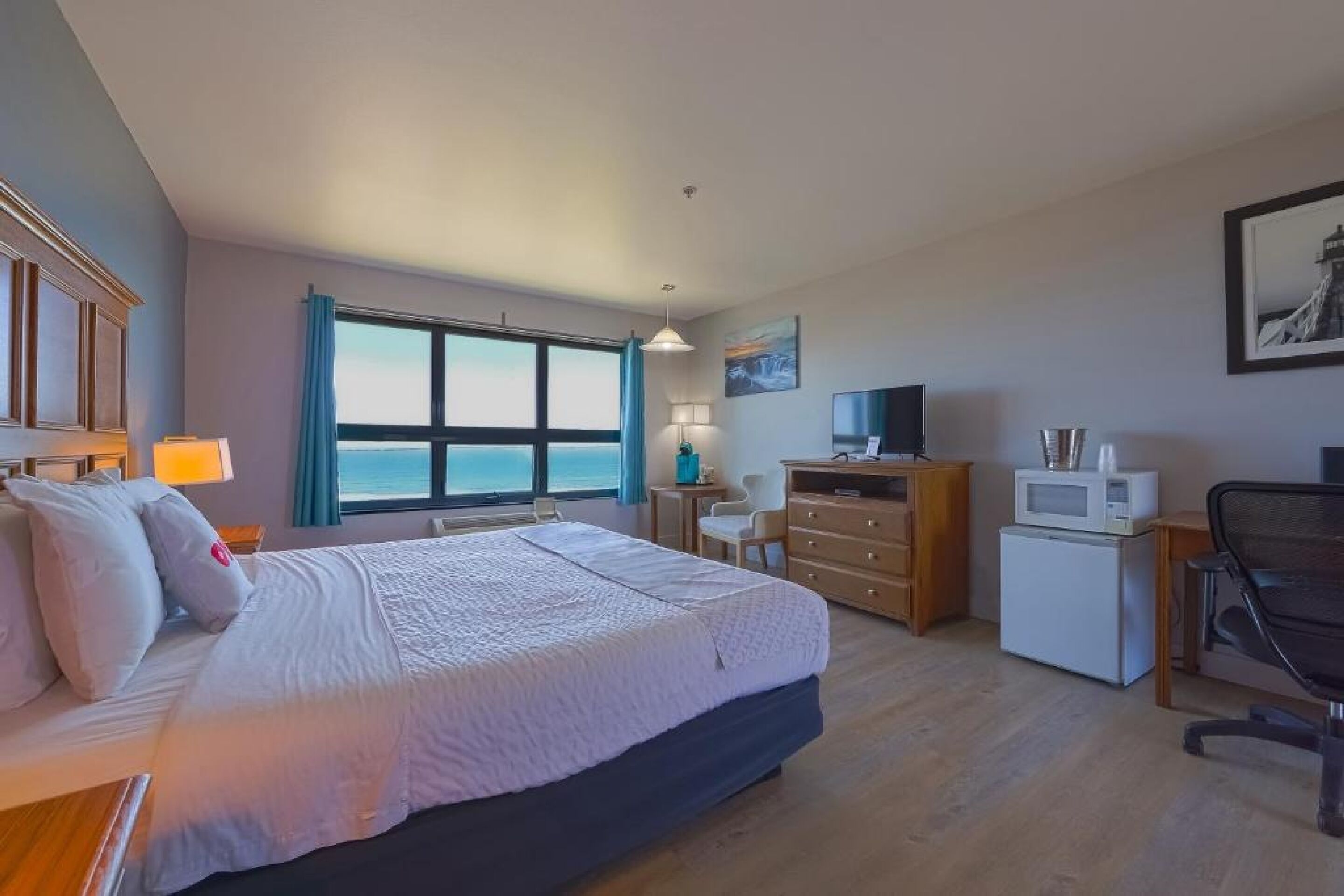 Habitación de hotel con una cama grande, un escritorio, una silla, un televisor, un microondas y vista al océano.