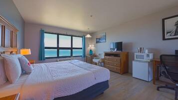 Habitación de hotel con una cama grande, un escritorio, una silla, un televisor, un microondas y vista al océano.