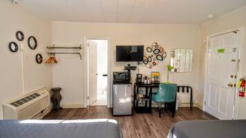 A compact hotel room with a bed, a desk with a computer, a TV, and a refrigerator.