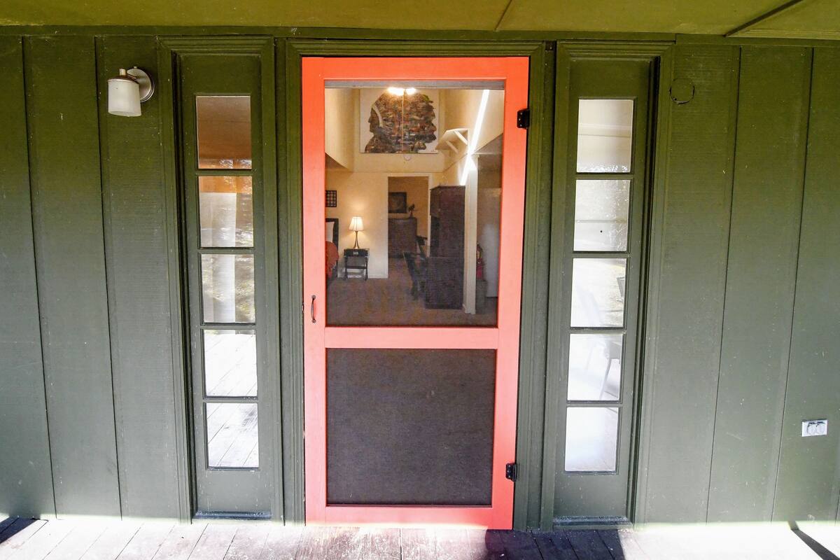 A green door with a red frame and a glass panel, leading to an interior with a lamp and a chair.
