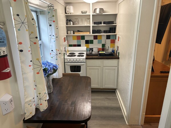 Una cocina compacta con armarios blancos, una encimera de madera, una estufa y un salpicadero de azulejos.