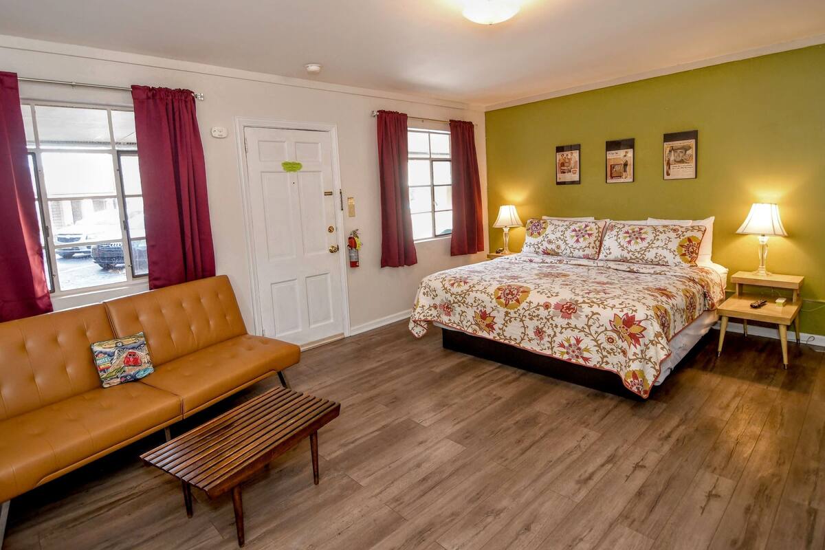A bedroom with a bed, a sofa, a bench, a nightstand, and a door.