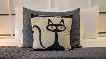 A bed with a quilted gray blanket, a pillow with a cat design, and a white headboard.