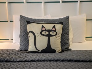 A bed with a quilted gray blanket, a pillow with a cat design, and a white headboard. - The Sunset Motel (Brevard)