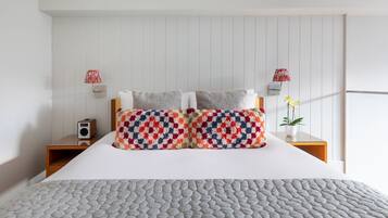 A neatly made bed with a patterned pillow, a bedside table with a lamp, and a wall-mounted speaker.
