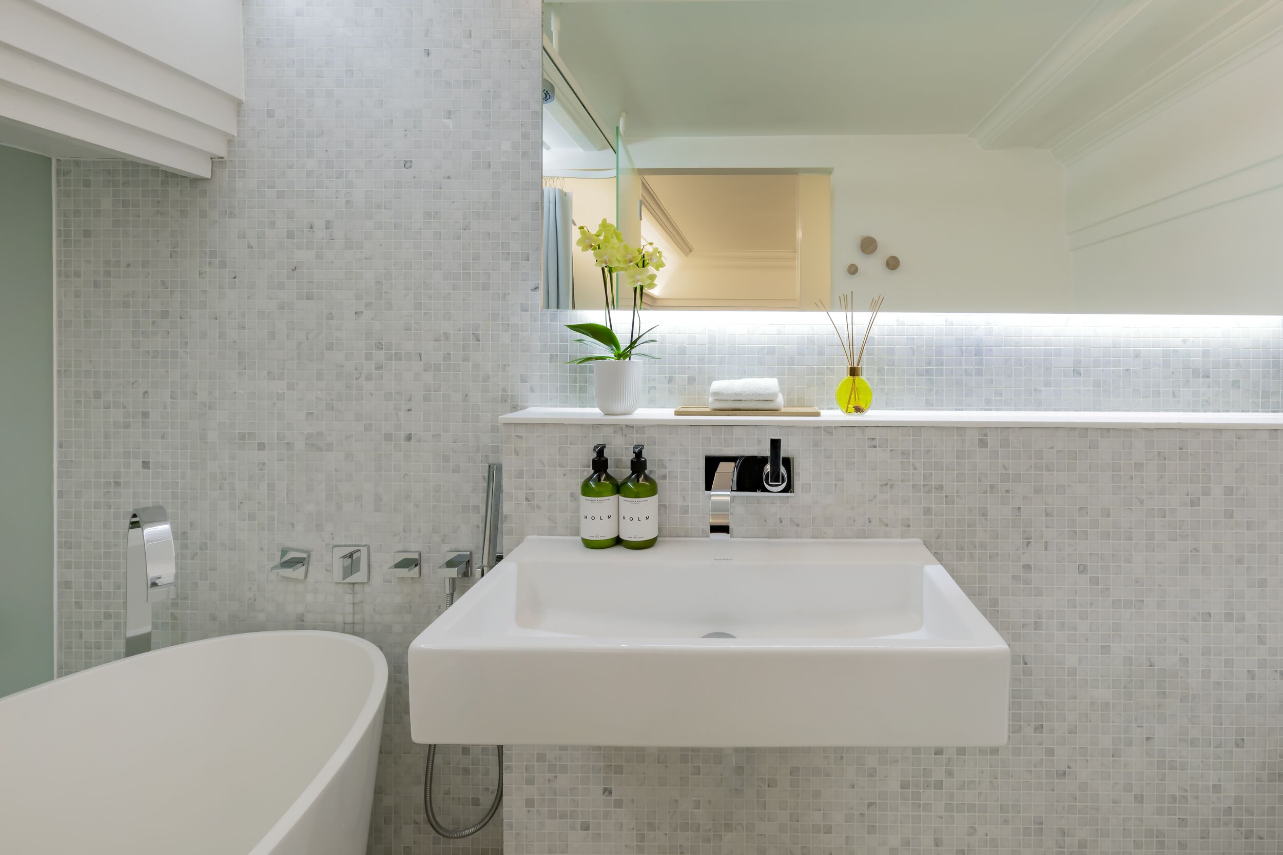 A modern bathroom with a freestanding bathtub, a white sink with two bottles of soap, and a mirror above the sink.