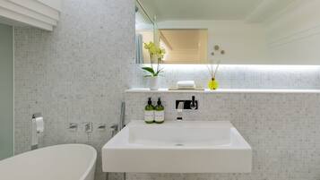 A modern bathroom with a freestanding bathtub, a white sink with two bottles of soap, and a mirror above the sink.