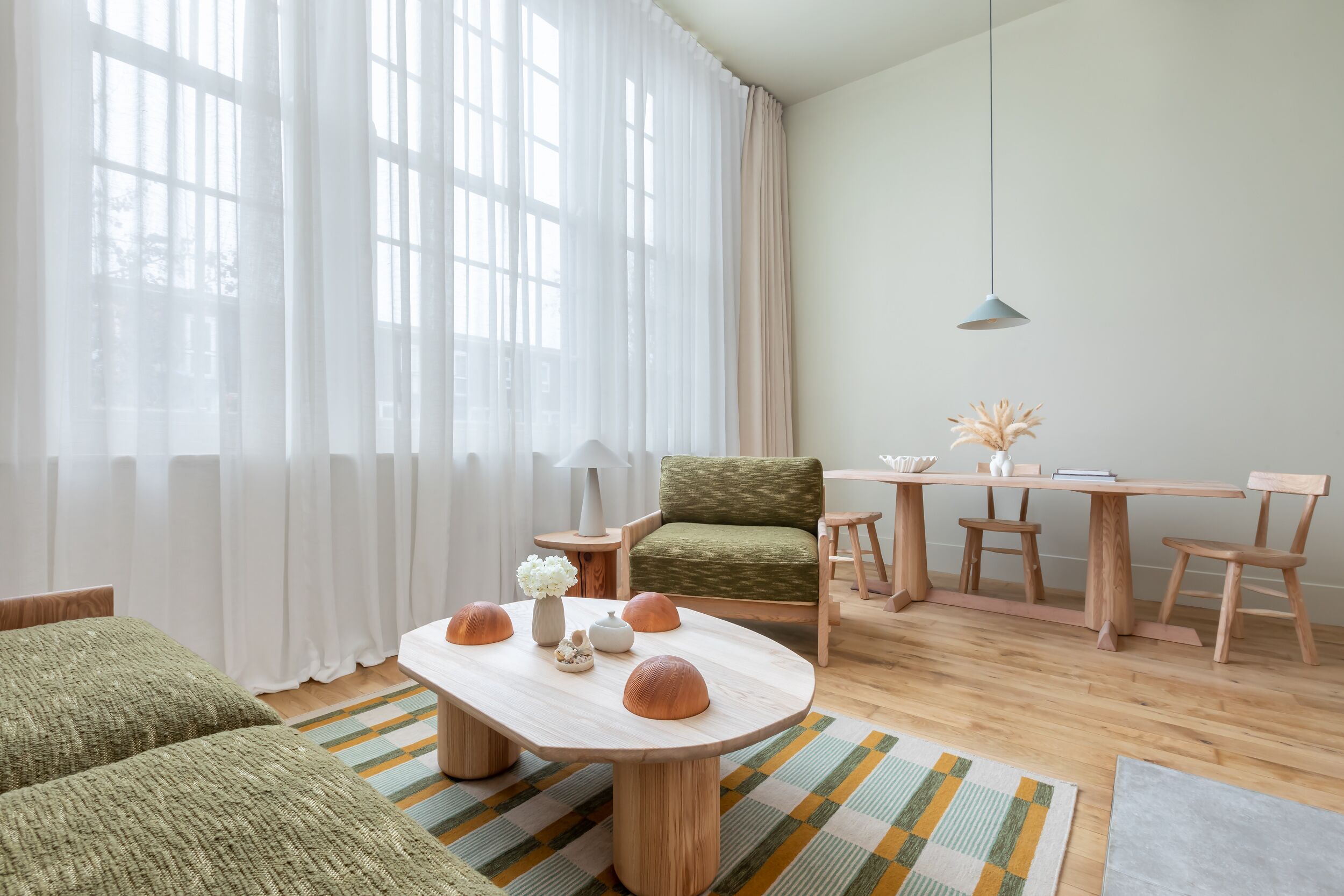 A modern living room with a wooden coffee table, green armchair, and a dining area with wooden chairs and a table.