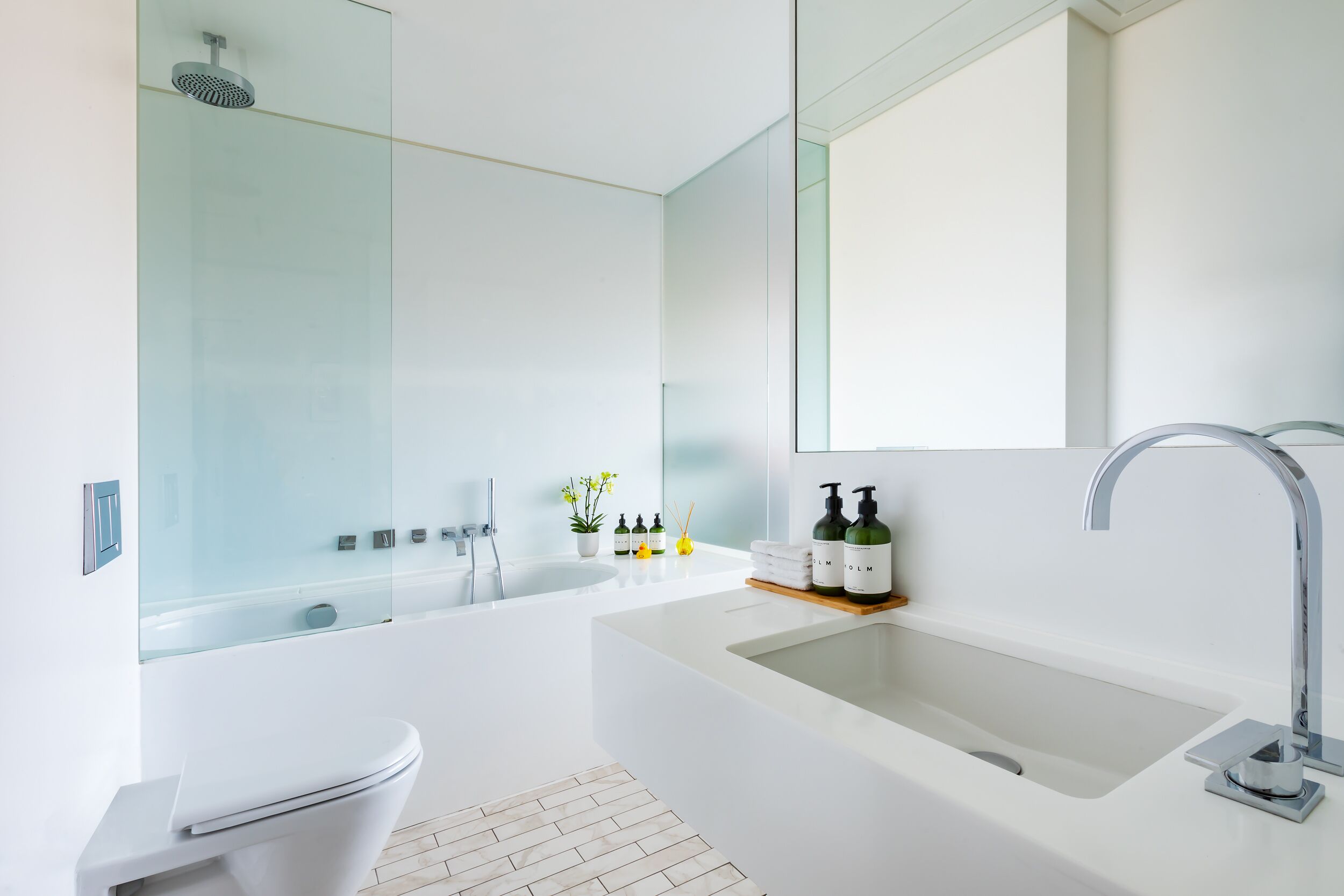 A modern bathroom with a glass-enclosed shower, a white bathtub, a sink with a large mirror, and toiletries on the countertop.