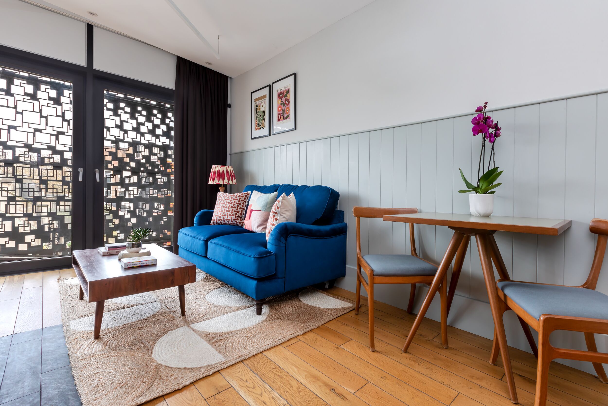 A modern living room with a blue sofa, wooden coffee table, and a dining table with chairs.
