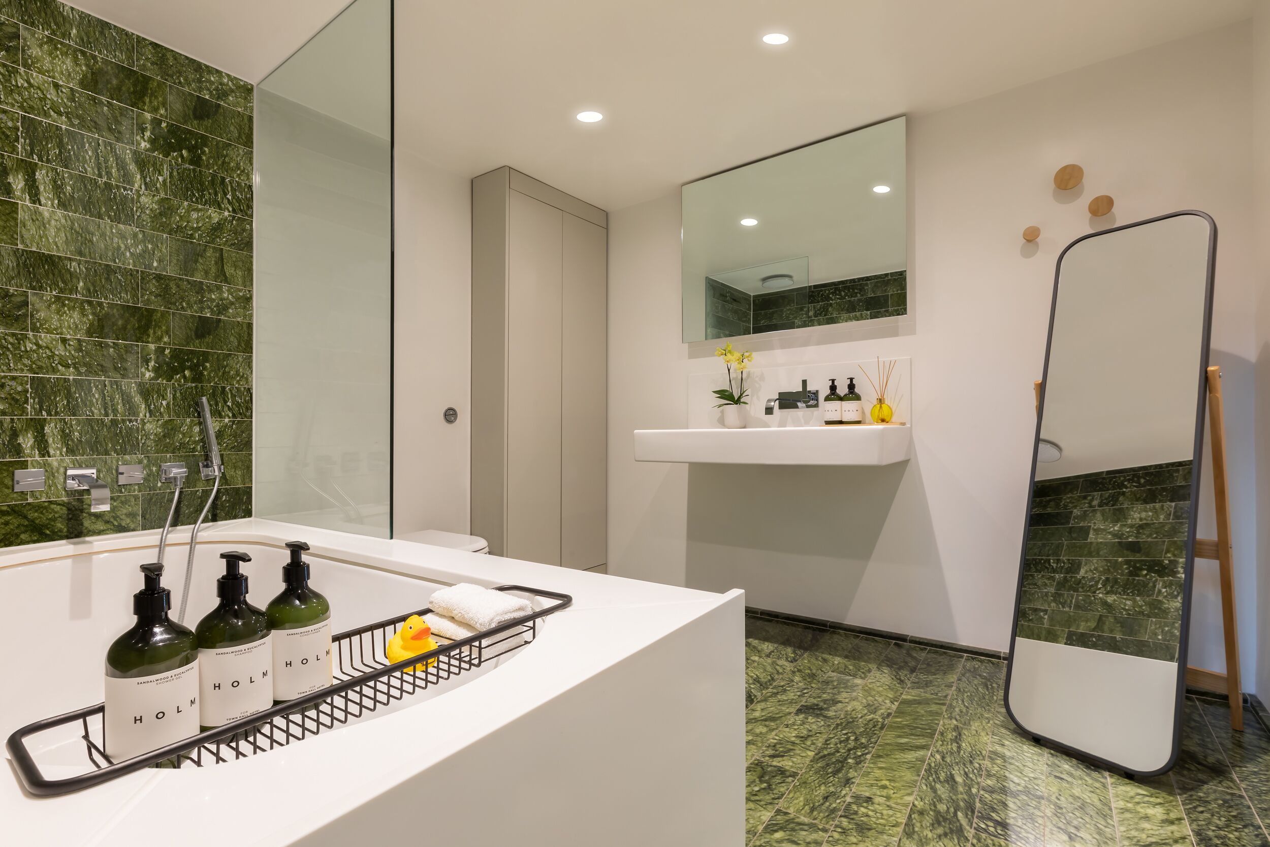 Un baño moderno con lavamanos blanco, espejo y azulejos de mármol verde.