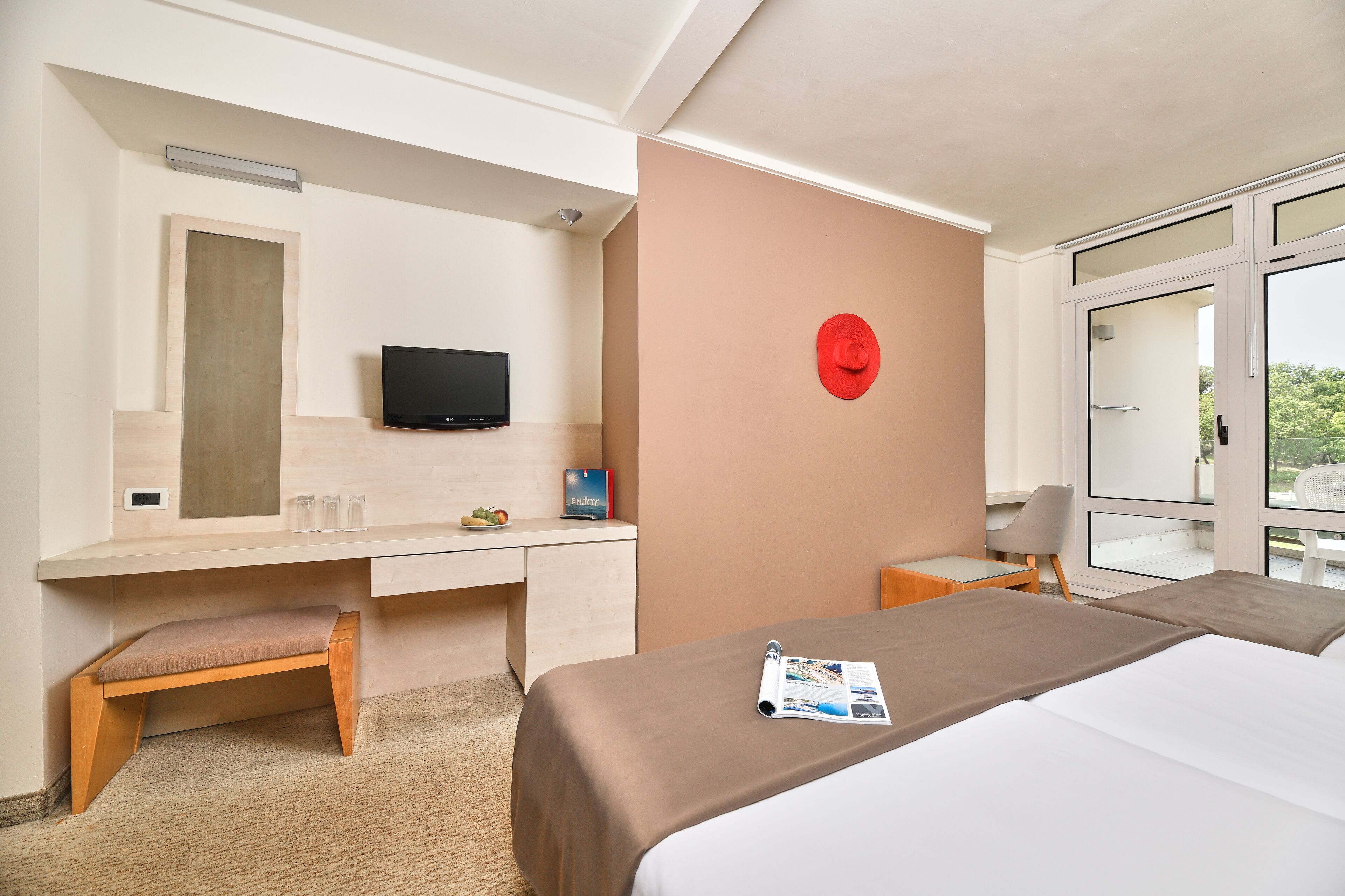 Une chambre d’hôtel moderne équipée d’un lit, d’un bureau avec une chaise, d’une télévision et d’une horloge murale rouge.