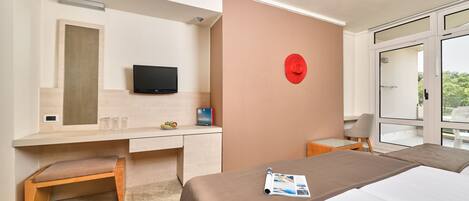 A modern hotel room with a bed, a desk with a chair, a television, and a red wall clock.