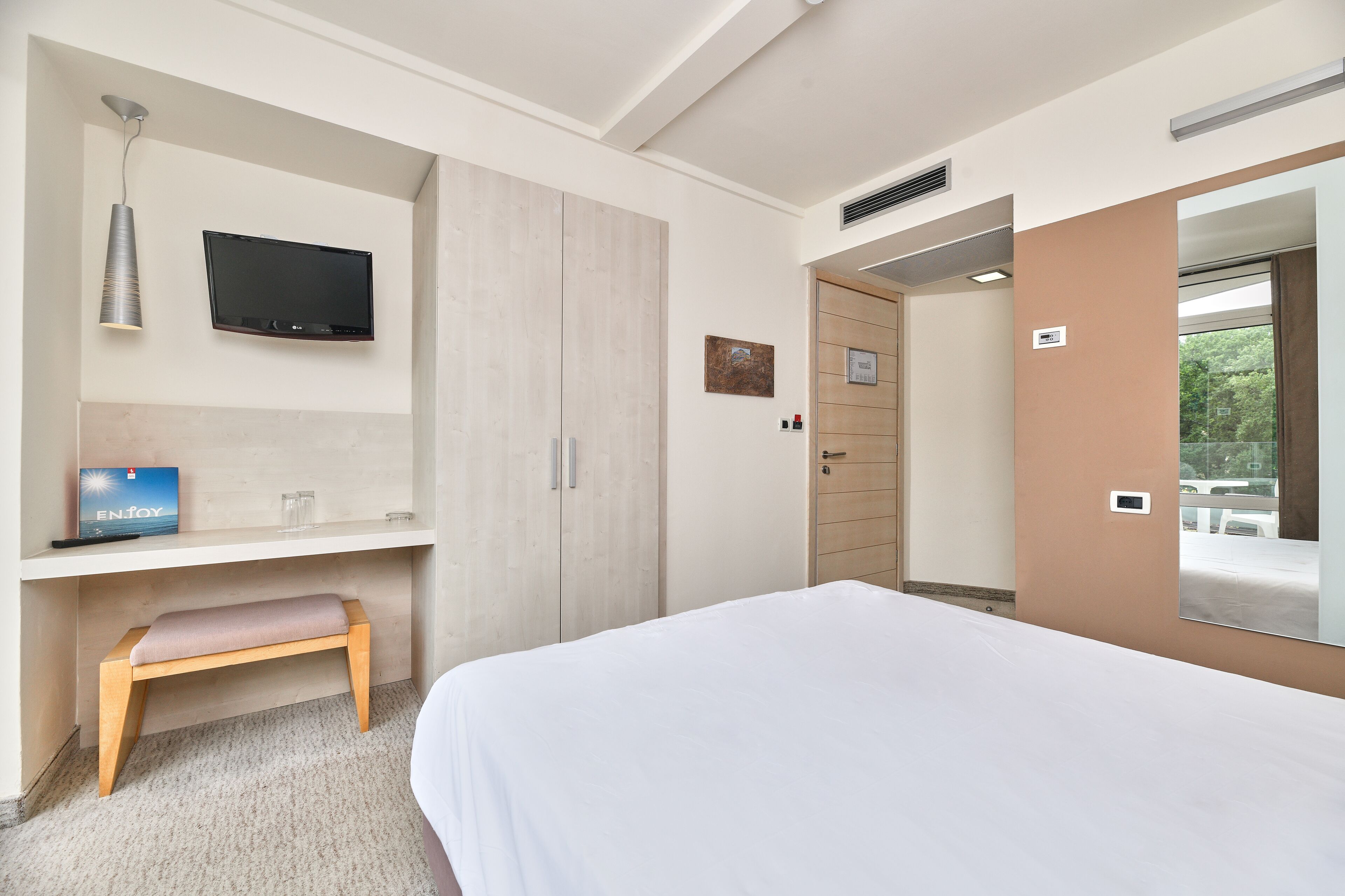 Una habitación de hotel moderna con una cama, un escritorio con una silla, un televisor y un armario.