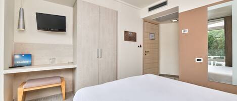 Una habitación de hotel moderna con una cama, un escritorio con una silla, un televisor y un armario.